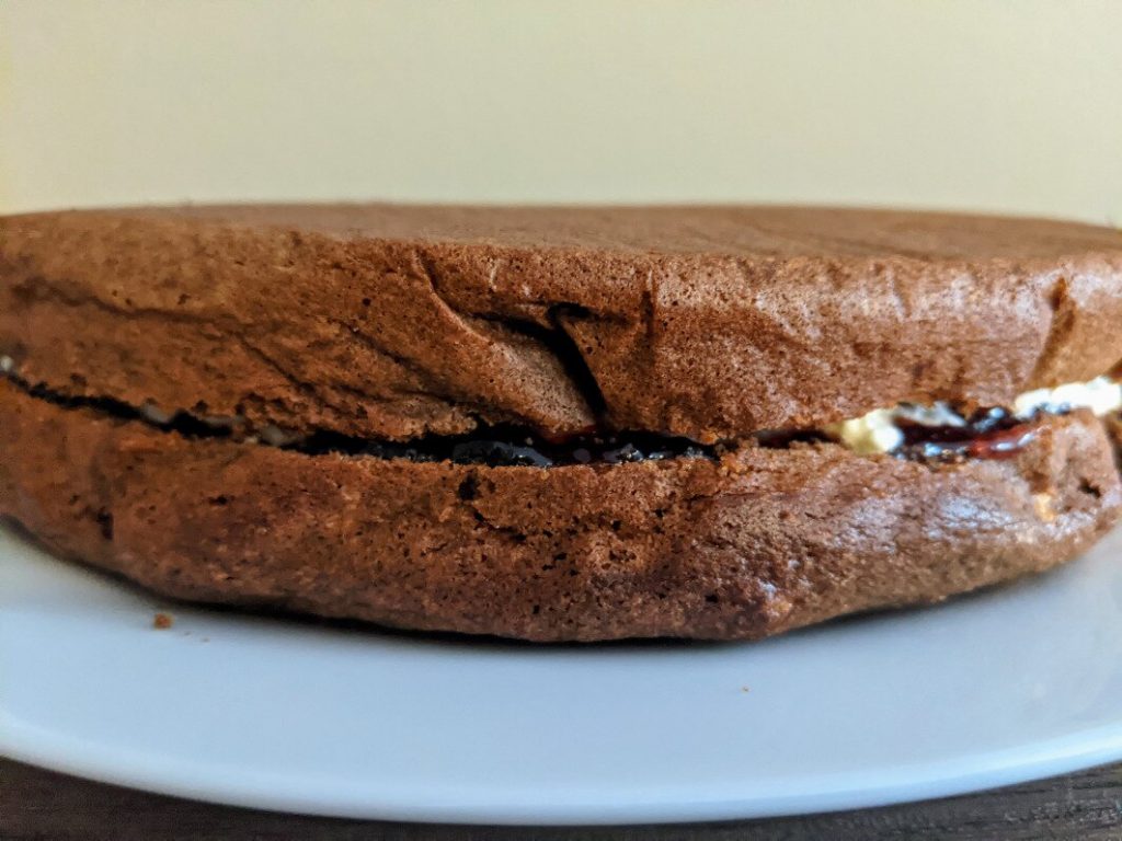 Ciasto kakaowe przekrojone na pół i posmarowane dżemem porzeczkowym i kremem.
